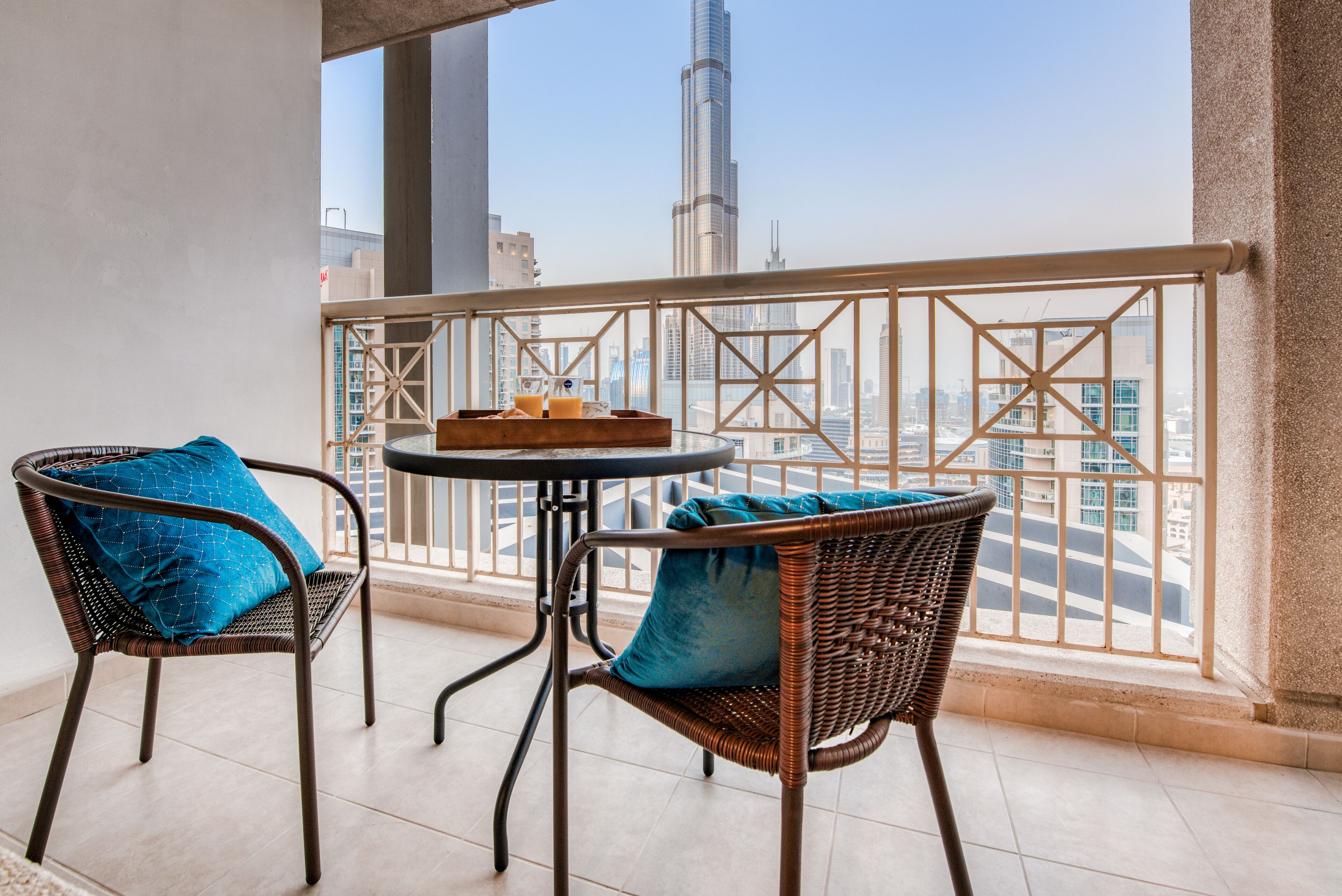 A balcony with two wicker chairs, a small round table, and a tray with drinks.