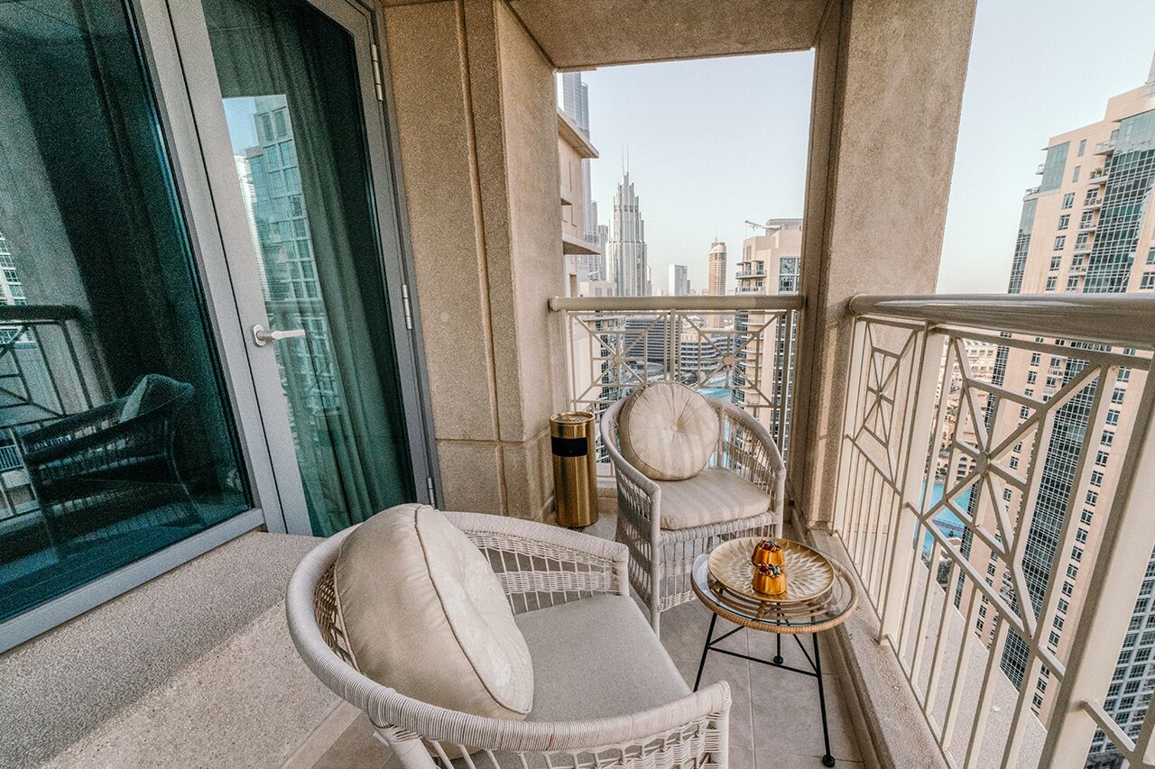 A balcony with wicker furniture, a small table, and a view of the cityscape.