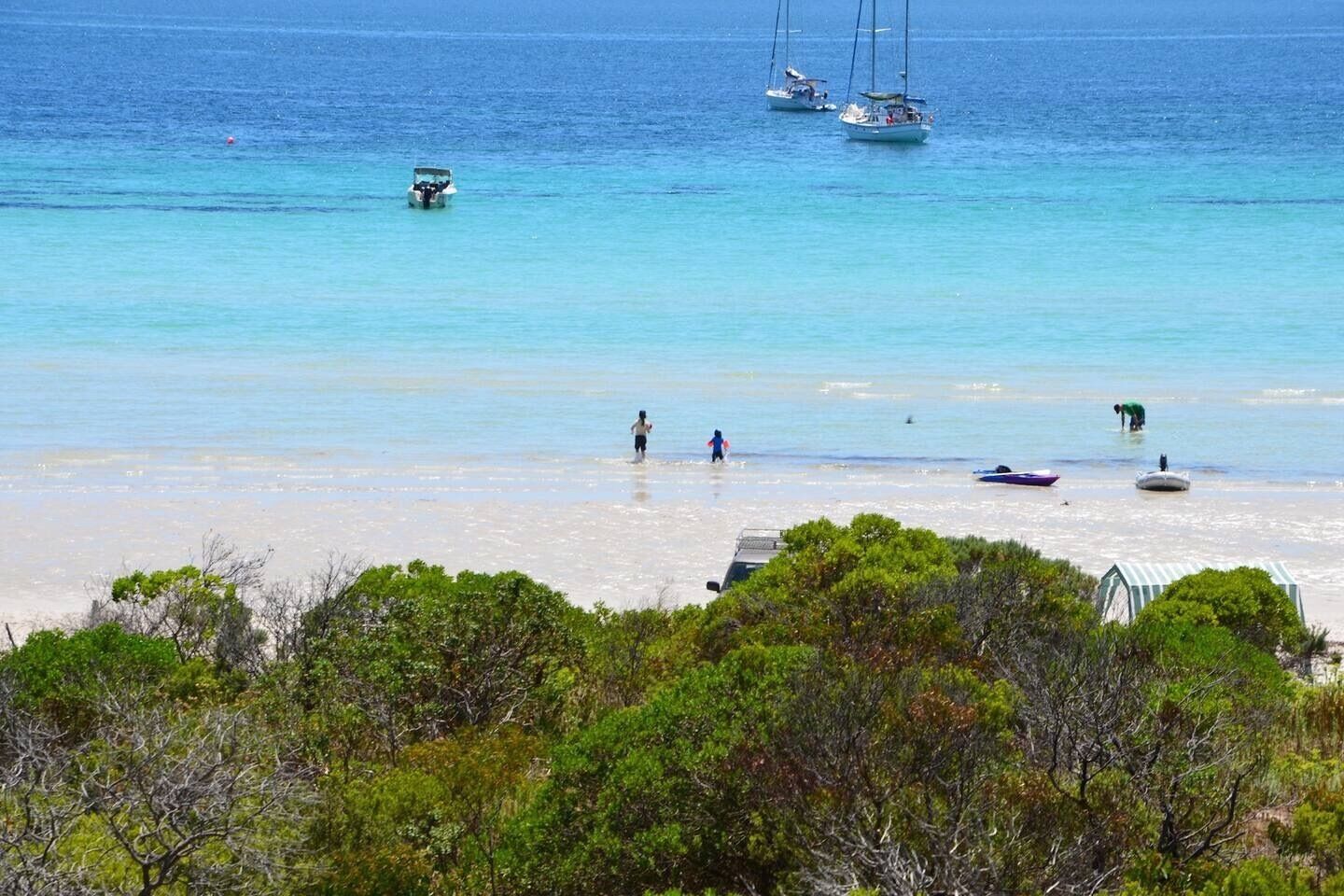 A beach with clear turquoise water, boats, and people.