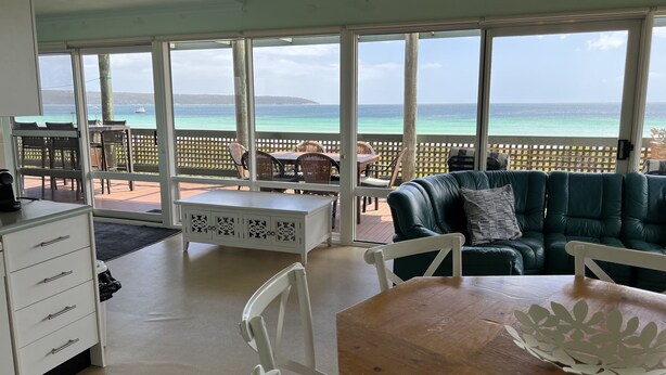 A room with a view of the ocean, a wooden table, a green sofa, and a white cabinet.