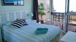 A bedroom with a bed, pillows, a nightstand, a lamp, and a view of the outside balcony.