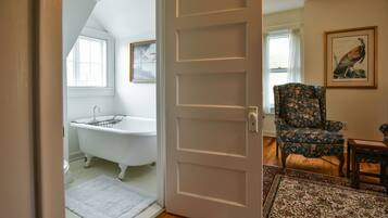A room with a white door, a bathtub, a floral armchair, and a rug.
