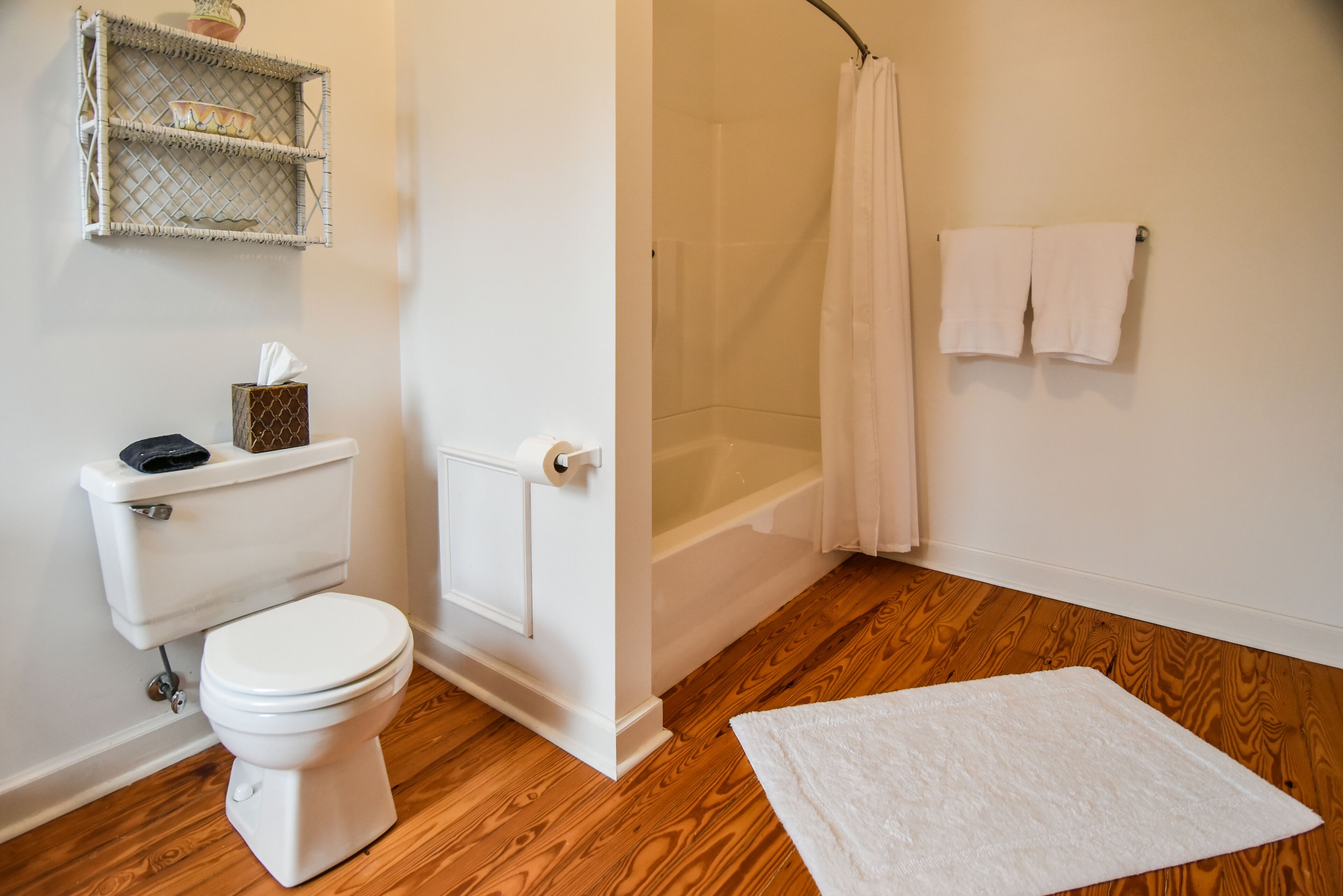 A bathroom with a toilet, shower, and a white rug on the floor.