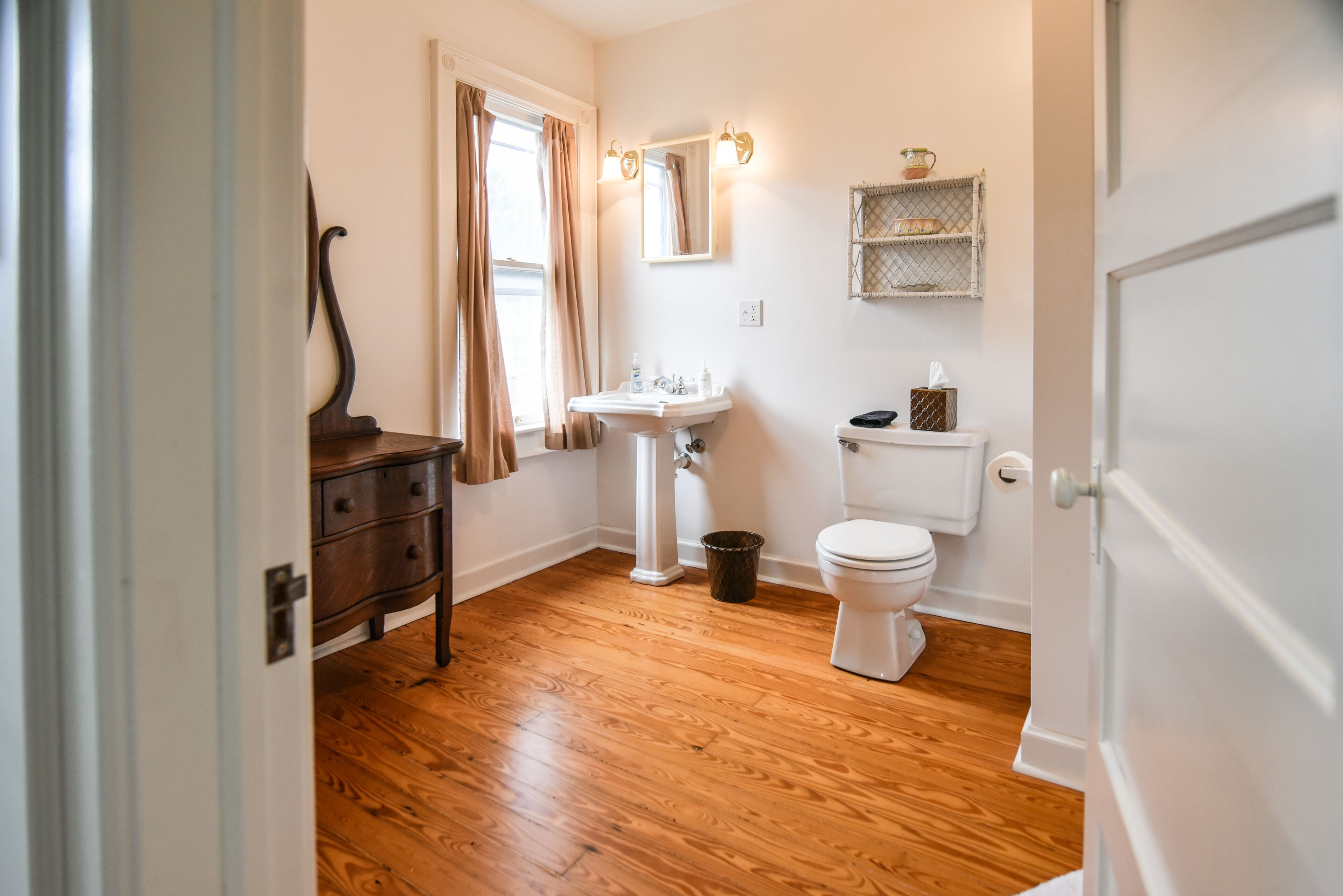Un baño con suelo de madera, un lavabo blanco, un inodoro y un aparador de madera oscura.