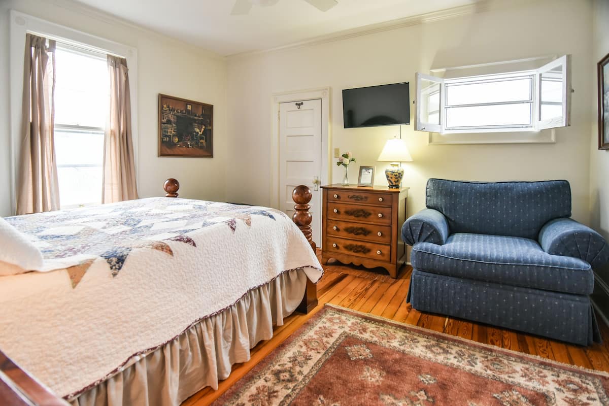 A bedroom with a bed, dresser, chair, and a television on the wall.