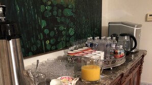 Un plan de travail de cuisine sur lequel on trouve divers objets, notamment une machine à café, une bouilloire, un panier de fruits et plusieurs verres.