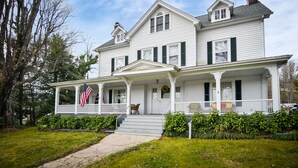Une maison blanche à deux étages, dotée d’un porche, d’un drapeau et d’une cheminée.