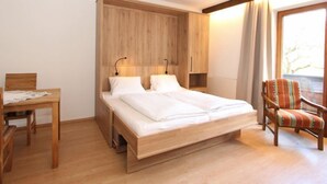A room with a wooden bed, a desk, a chair, and a window with curtains. - Römerhof by Interhome (Fügen)