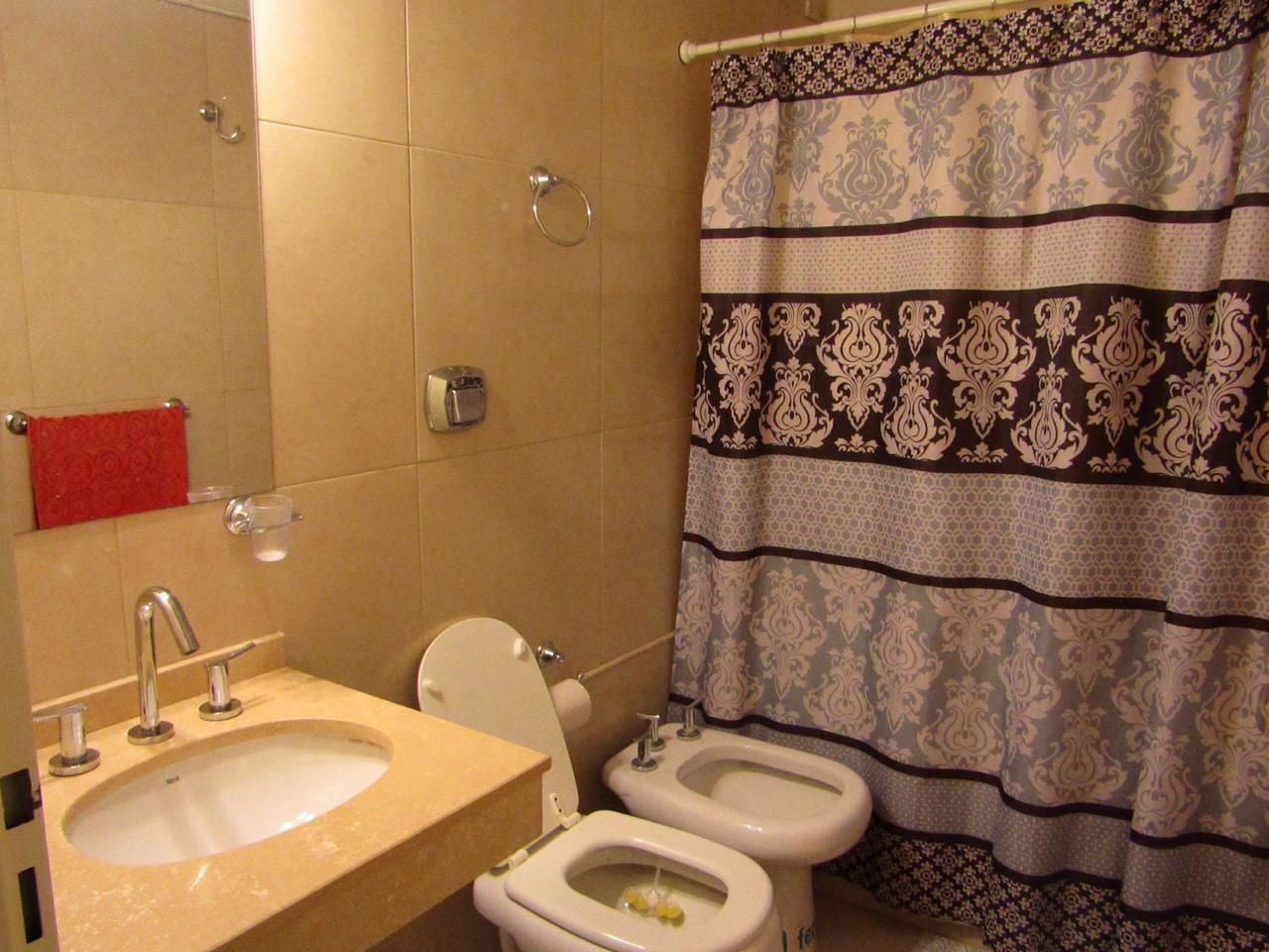 A bathroom with a sink, two toilets, a mirror, and a patterned shower curtain.