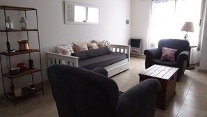A living room with a sofa, armchairs, a coffee table, a bookshelf, and a window with curtains. - Casa Nebel - Duplex (Concordia)