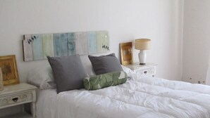 A neatly made bed with white bedding and two pillows, a bedside table with a lamp, and a wall with a bird painting. - Casa Nebel - Duplex (Concordia)