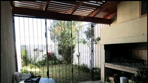 A patio area with a round table and chairs, a grill, and a view through a metal gate to a garden. - Casa Nebel - Duplex (Concordia)