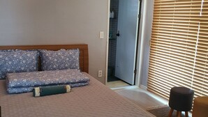 Un dormitorio con cama, mesita de noche, luz empotrada en la pared, una puerta y una ventana con persianas.