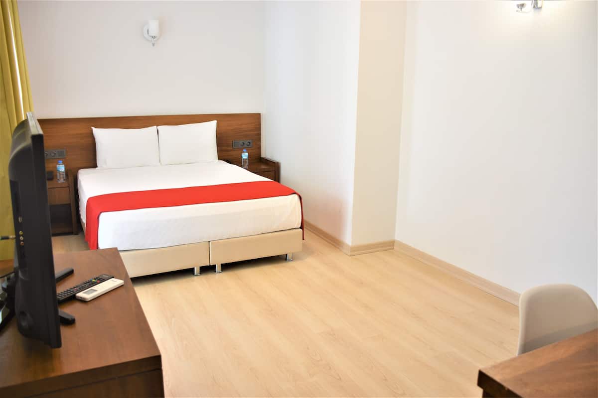 Habitació d'hotel amb llit, taules de nit, escriptori amb ordinador i una cadira.