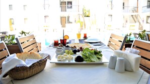 Una mesa dispuesta con diversos alimentos, como pan, queso, aceitunas y verduras, con vistas a edificios al fondo.