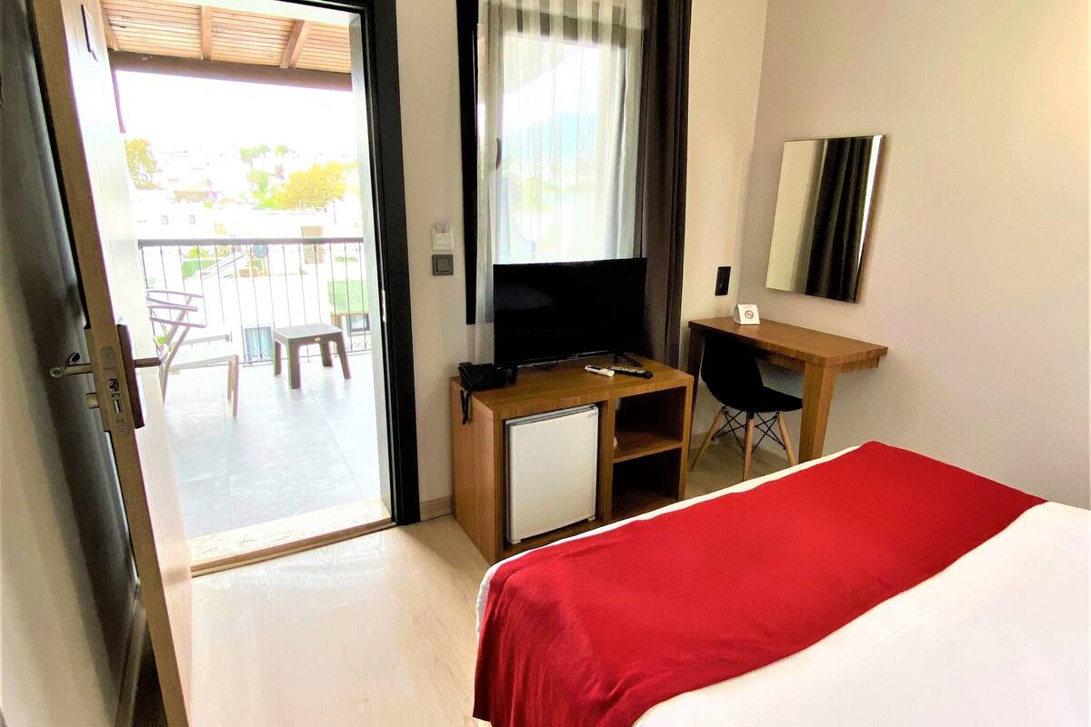 Habitació d'hotel amb llit, escriptori amb ordinador, televisió i nevera petita.