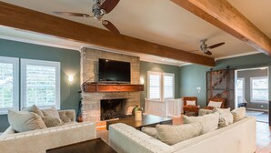 A living room with a fireplace, wooden beams, a ceiling fan, and a television.