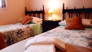 A hotel room with two beds, each with a patterned bedspread and pillows. There is a nightstand with a lamp between the beds. - Buenos Aires 212 (Salta)
