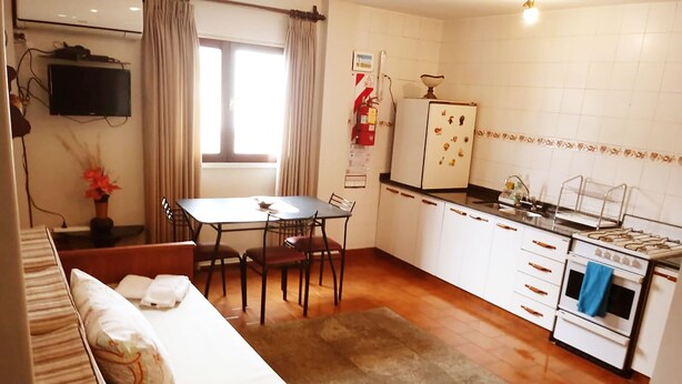 A compact hotel room with a bed, a dining table with chairs, a kitchenette with a stove and refrigerator, and a TV mounted on the wall. - Buenos Aires 212 (Salta)