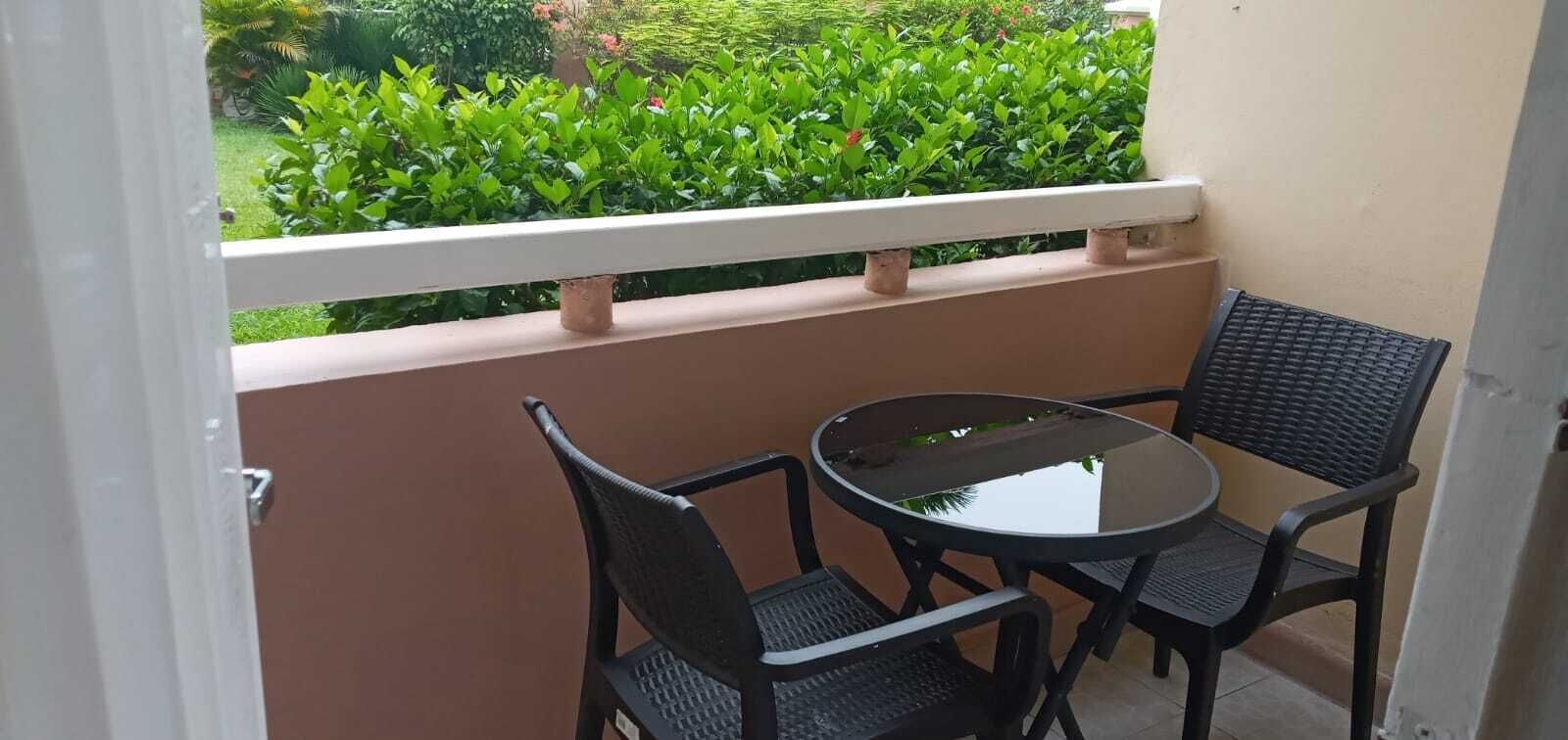 A small balcony with a round table and two chairs, surrounded by a white railing.