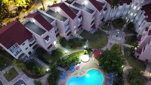 An aerial view of a residential complex with a central swimming pool surrounded by lounge chairs, a parking area, and a street with parked cars. - Luxe Beach Front Retreat (Ocho Rios)