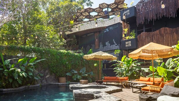 A poolside area with stone seating, umbrellas, and lush greenery. - Maka Hotel Boutique (Tulum)