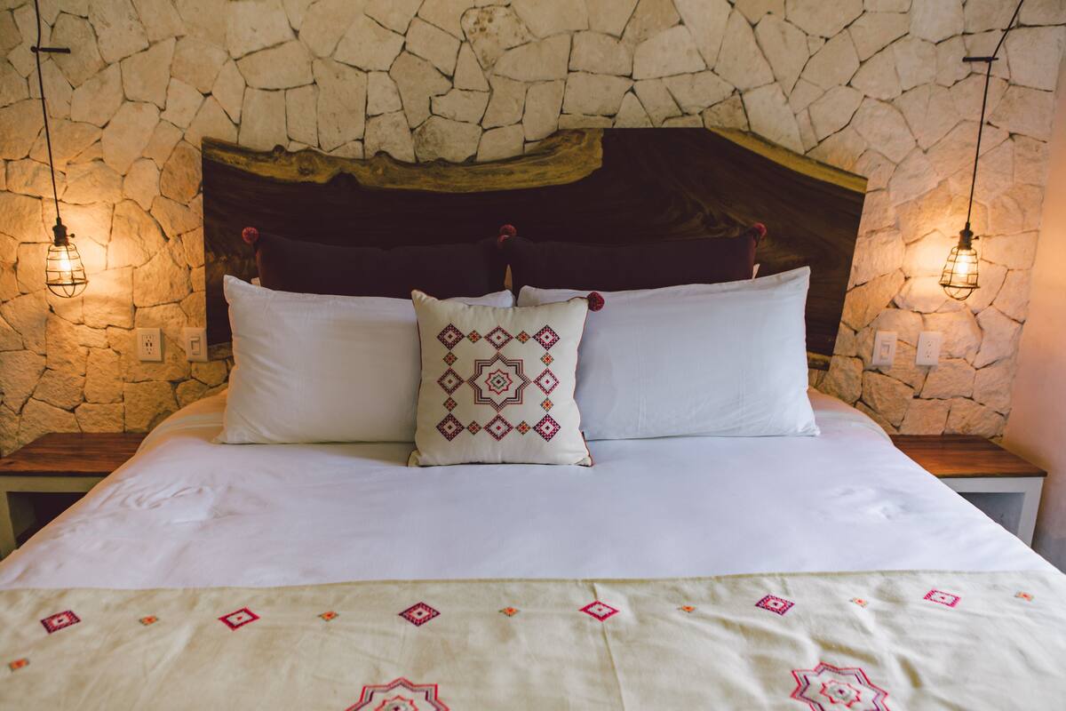 Ein Bett, das an einer Steinwand steht, mit zwei Nachttischen und einer dekorativen Decke.