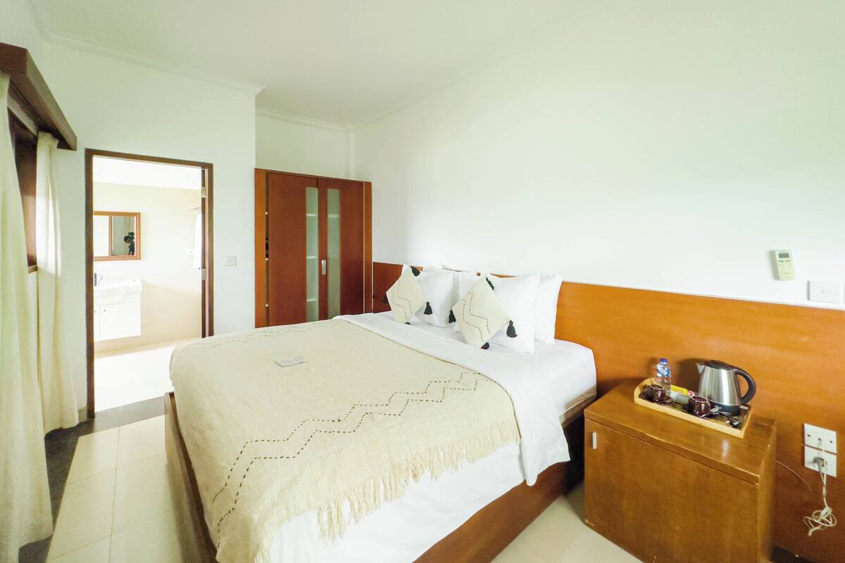 A hotel room with a bed, a wooden nightstand, a mirror, and a wardrobe.