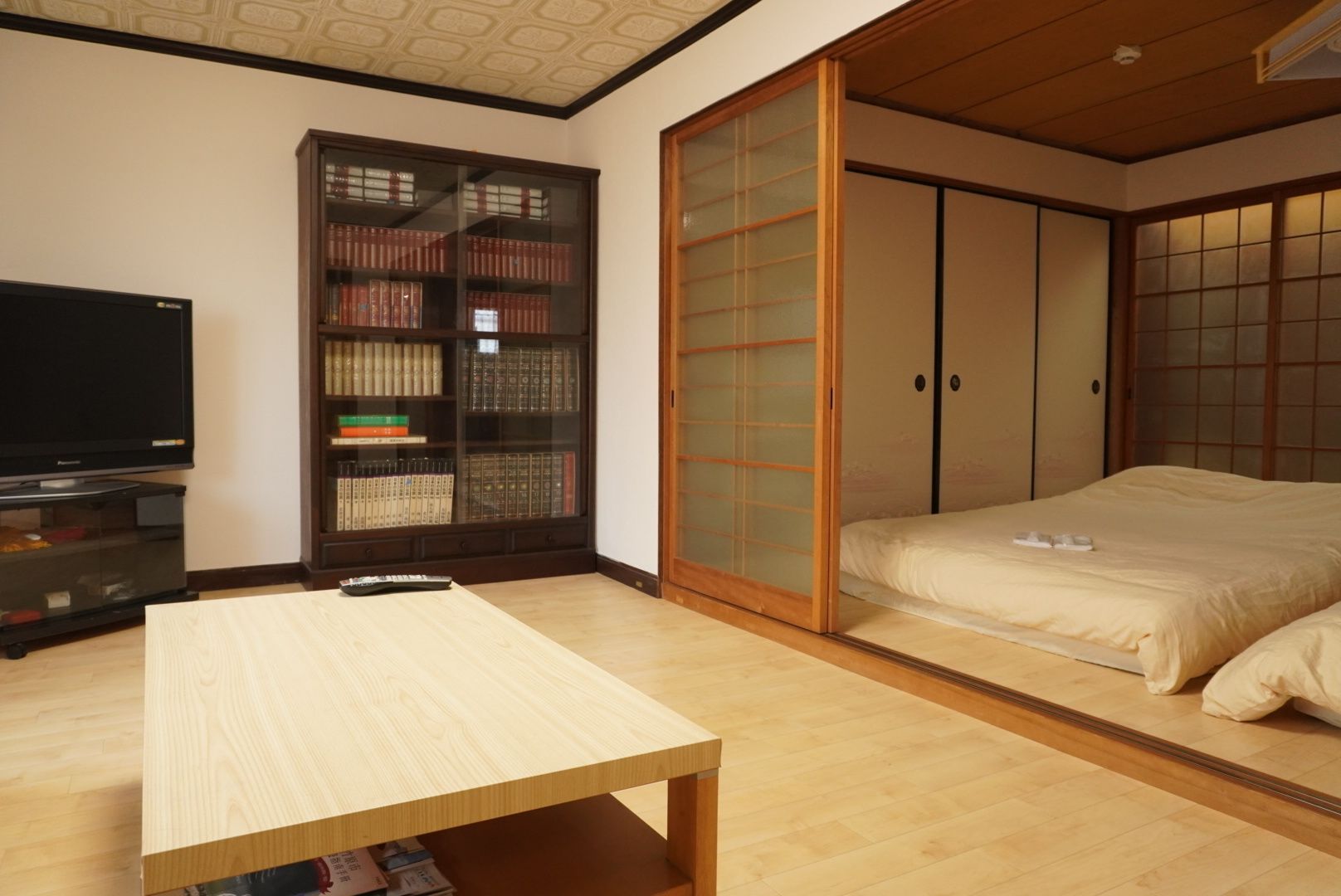 Une pièce de style japonais traditionnel, avec un sol recouvert de tatamis, une petite table en bois, un téléviseur et un placard à portes coulissantes.