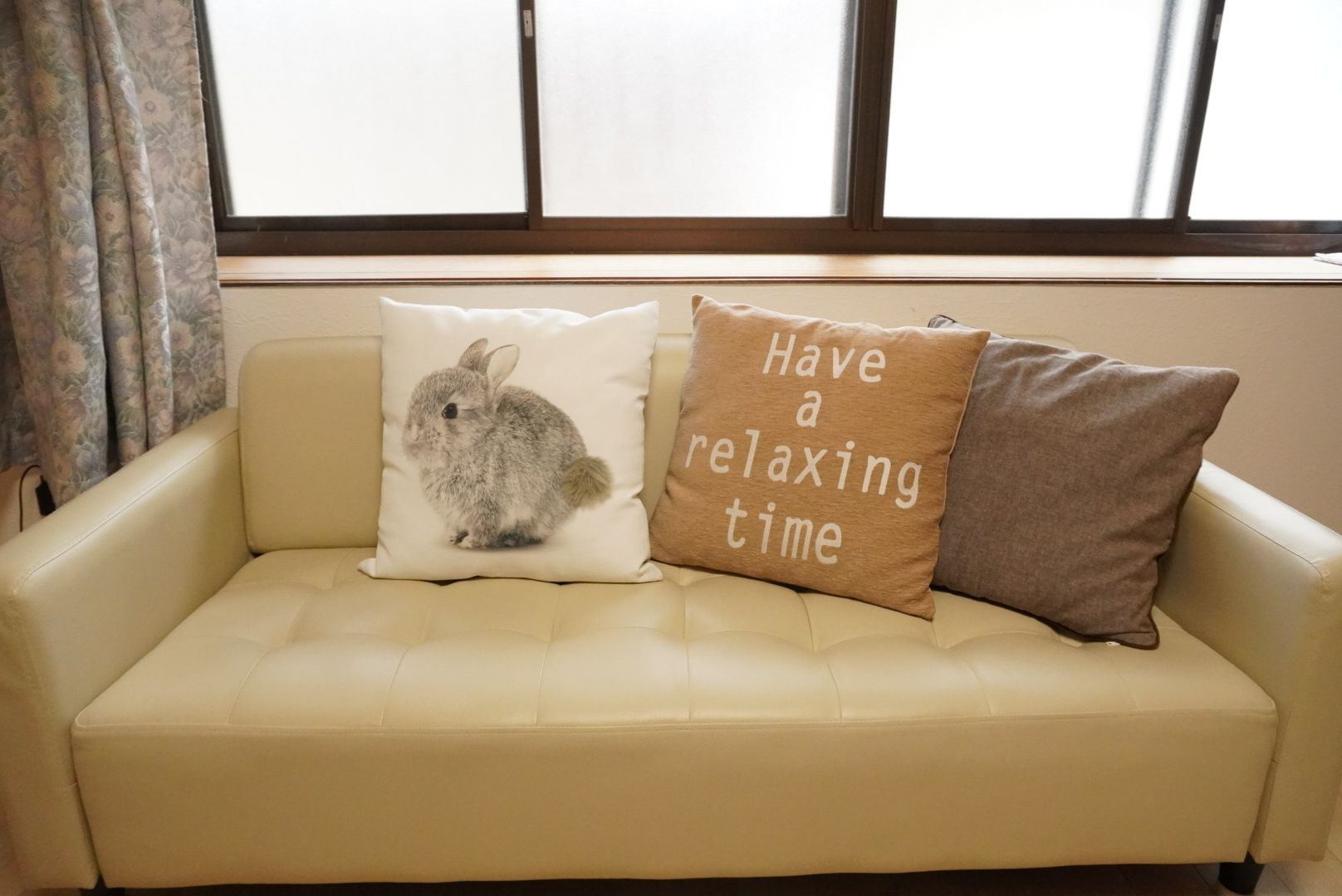 A beige sofa with two decorative pillows, one with a rabbit illustration and another with text.