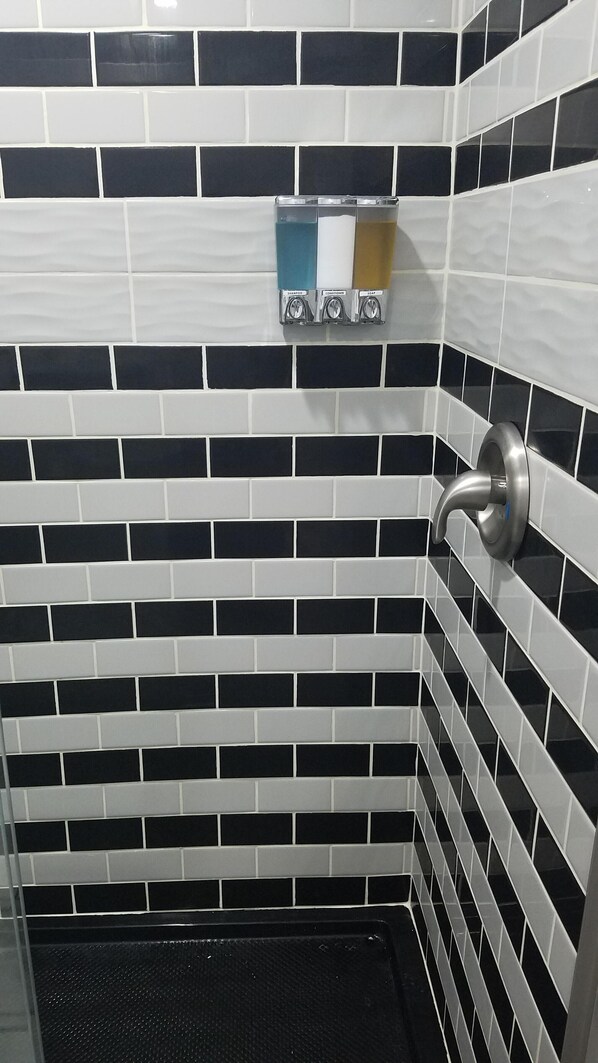 A bathroom with black and white tiled walls, a shower area, and a soap dispenser mounted on the wall.