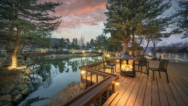 A wooden deck with a fire feature, seating, and a pond.