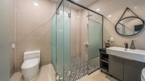 A modern bathroom with a glass-enclosed shower, a toilet, and a sink with a mirror above it. - May Garden (Gangneung)
