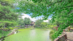 A serene park with a pond, wooden deck, and a building with a traditional architectural style.