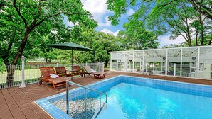 A swimming pool with a wooden deck, lounge chairs, and a covered seating area.