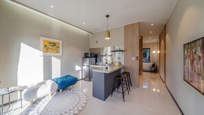 A modern kitchen with a central island, a dining area with a sofa and chairs, and a living area with a large window. - May Garden (Gangneung)