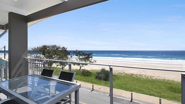 Un balcón con mesa y sillas de vidrio con vista a una playa.