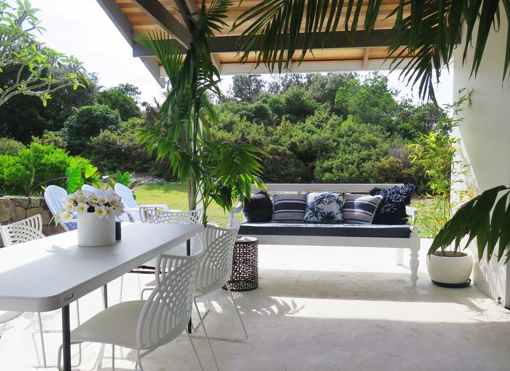 An outdoor patio with a white table and chairs, a black and white patterned sofa, and potted plants.