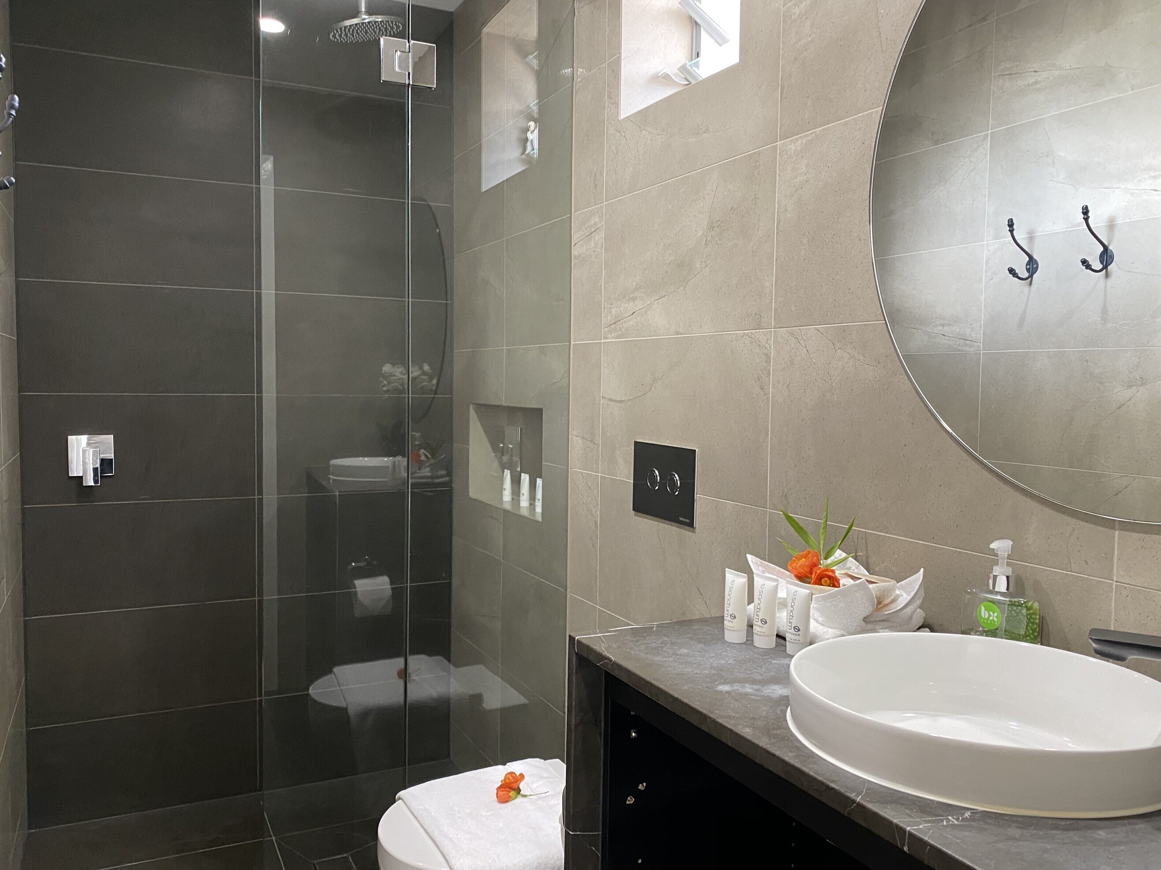 A modern bathroom with a glass-enclosed shower, a round mirror, and a vanity with a sink.