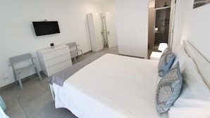 Un dormitorio con cama, escritorio, silla, televisor y vestidor.