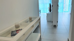 Una habitación de hotel moderna con un escritorio de vidrio, una banca, una taza de café y un libro titulado "The Partner".