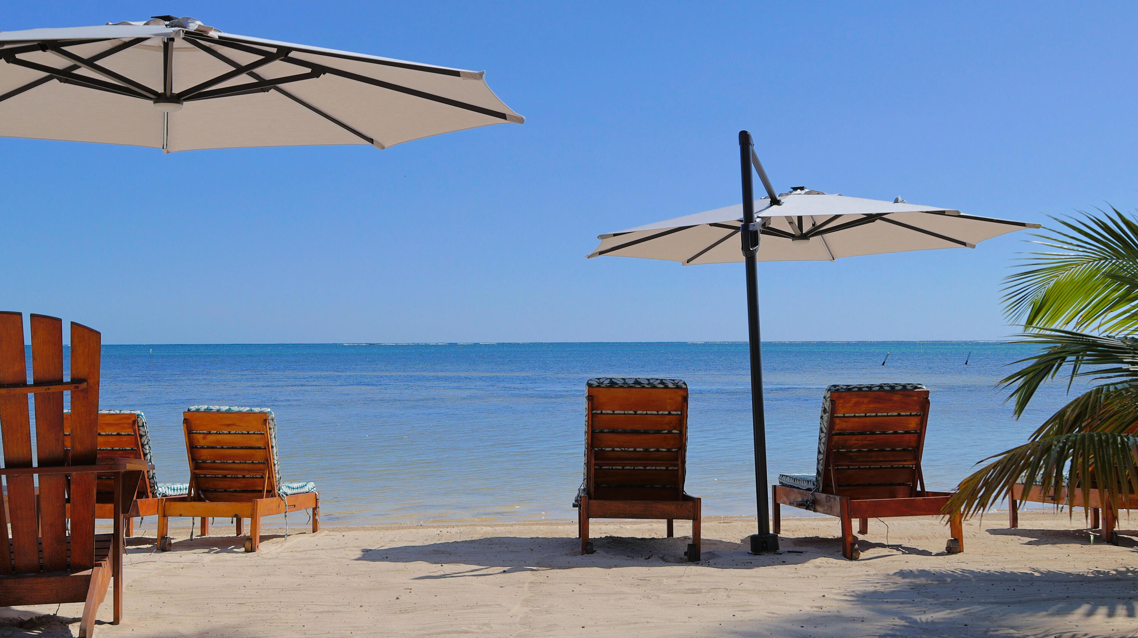 Ein Strand mit Holzliegen und zwei Sonnenschirmen, die Schatten spenden.