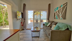 A living room with a sofa, a coffee table, a TV, and a view of the beach through a sliding door. - Mangata Villas (San Pedro)