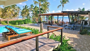 A poolside area with lounge chairs, a wooden deck, and a view of the beach and ocean. - Mangata Villas (San Pedro)