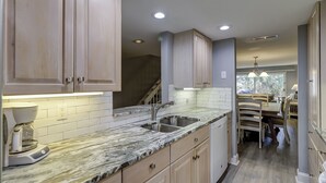 A modern kitchen with marble countertops, wooden cabinets, and a built-in sink. - Sunset Rentals | Shipmaster 1602 | Dog Friendly (Hilton Head Island)