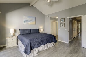Un dormitorio con cama, mesitas de noche, un cuadro y un pasillo.