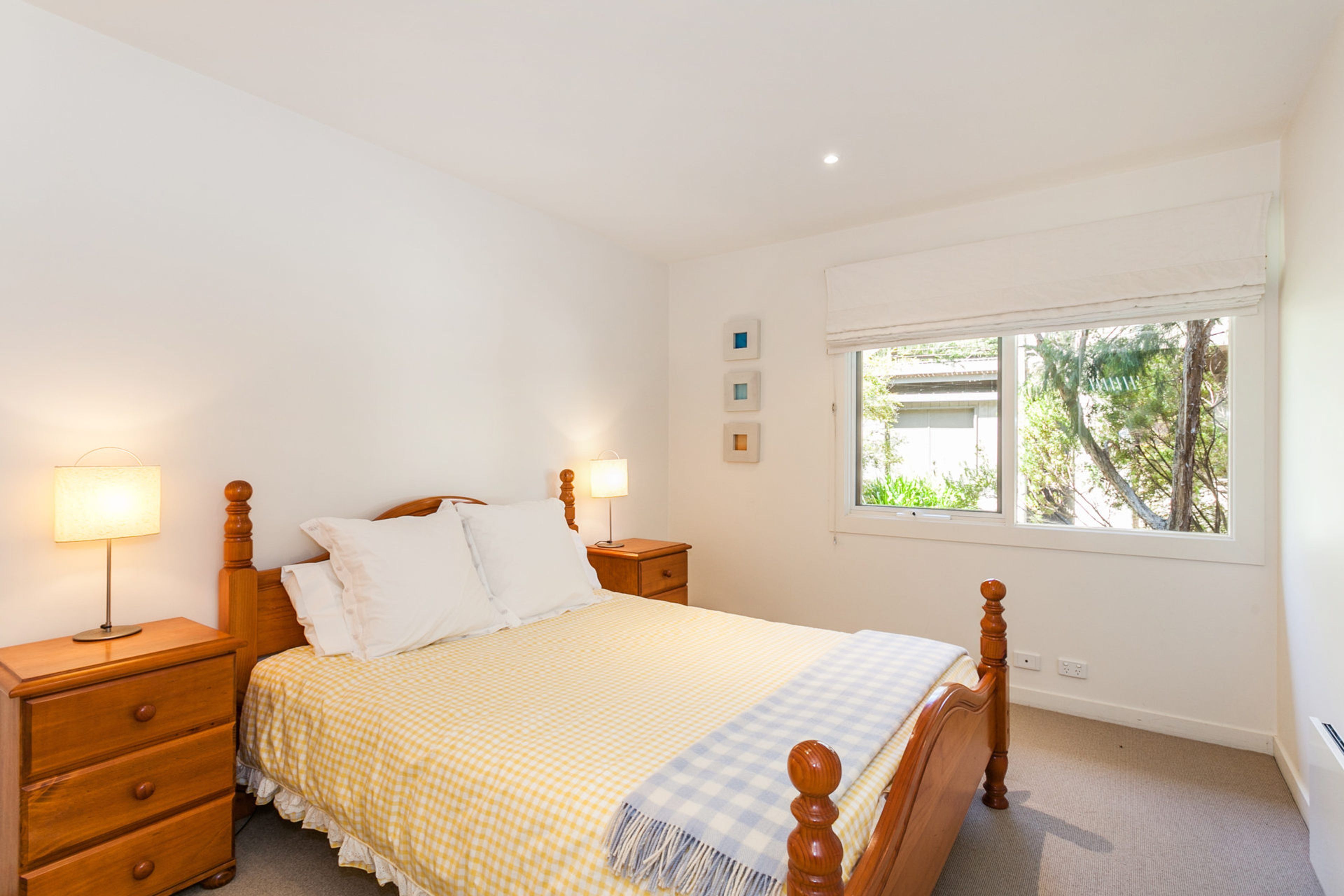 Quarto com uma cama de solteiro, duas mesas de cabeceira, uma janela com vista para o verde e um interruptor de luz fixado na parede.