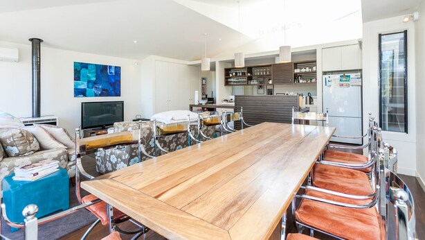A modern kitchen with a large wooden table, built-in cabinets, and a flat-screen TV. - Breaker Eight (Lorne)