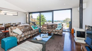 A modern living room with a large window, a fireplace, and a dining area. - Breaker Eight (Lorne)