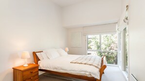 A bedroom with a wooden bed, a nightstand, a window with a view of greenery, and a wall-mounted artwork. - Breaker Eight (Lorne)